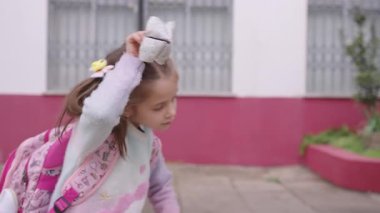 Sırt çantalı kız okul dışında yürürken kağıt falcıyı gösteriyor. Kız kağıt oyuncağı tutarken neşeyle gülümsüyor, zamanının tadını çıkarıyor.