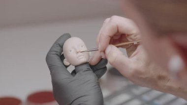 Sanatçı ince fırça kullanarak silikon bebek kafasına ince detaylar ekliyor, minyatür figür oluşturmada ustalığı ve ustalığı vurguluyor