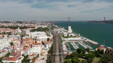 Portekiz 'deki Lizbon rıhtımında gezinen İHA, liman, şehir sokakları ve 25 de Abril Köprüsü' nü gösteriyor. Sakin mavi nehir, tarihi simgeler ve berrak gökyüzü, seyahat ve keşif çağrıştırıyor.