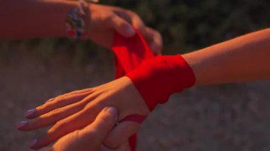 Gün batımında kumsalda kadın boksörün eline kırmızı boks örtüsü takan sportif bir kadın. Doğa antremanına hazırlanan boksör ve antrenörün yakın çekimi