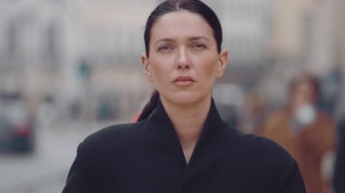 Şehir caddesinde ciddi bir yüzü olan, siyah ceketli, önüne bakan, insanlarla ve binalarla geçmişi bulanık, kentsel yaşam tarzı konseptiyle kendinden emin genç bir kadın.