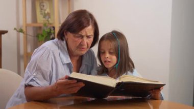 Büyükanne ve torun birlikte masa başında oturup kitap okuyor, evde öğrenme, sevgi ve aile bağlarını paylaşıyorlar.
