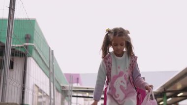 Sırt çantalı ve beslenme çantalı kız okuldan birkaç adım ötede, dersten sonra rahat bir ifadeyle oradan ayrılıyor.