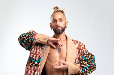 Rahatlamış sakallı Afro-Amerikan eşcinsel adam meditasyon sırasında rahatlıyor, renkli bir ceket giyiyor, yoga yapıyor, temiz hava soluyor, beyaz stüdyo arka planında izole edilmiş.