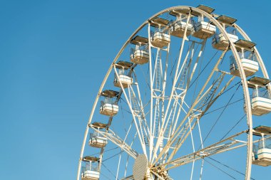 Büyük dönme dolap parlak mavi gökyüzüne karşı duruyor, beyaz yapısını ve gondollarını sergiliyor..
