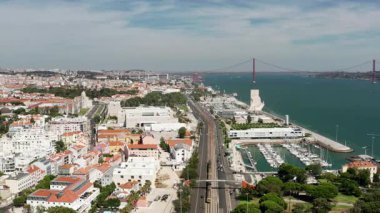 25 de Abril Köprüsü, demiryolu rayları, Tagus Nehri boyunca marina ve şehir manzarasının yer aldığı Lizbon liman manzarası açık güneşli bir günde kentsel ve kıyı uyumunu gösteriyor
