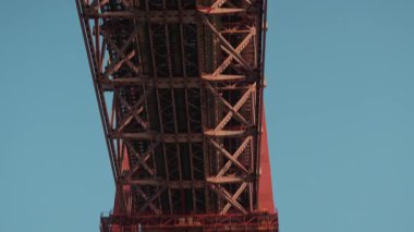 Aşağıdan 25 Nisan 'da Lizbon' da bulunan büyük bir metal köprünün çarpıcı görüntüsü, mühendislik ve tasarımı vurgulayarak, parlak mavi gökyüzüne karşı yapısal detaylarını vurguluyor..