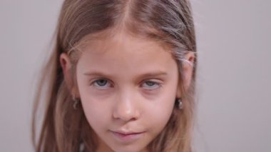 Uzun saçlı ve yüzünde ciddi bir ifade olan genç bir kız. Sakince kameraya bakıyor. Sade bir arka planı var. Basit bir stüdyo ışığı.