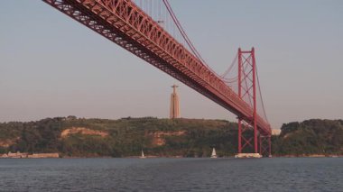 Gün batımında güzel aydınlatılan büyük bir asma köprünün nefes kesici görüntüsü, suya tepeden bakan bir İsa heykeli, huzurlu bir atmosfer yaratıyor..