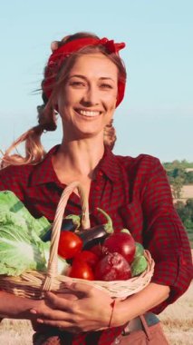 Kırmızı ekose gömlekli bir kadın gururla elinde canlı sebzelerle dolu bir sepet tutuyor. Domates, patlıcan ve marul gibi. Güneşli günün tadını çıkarıyor..