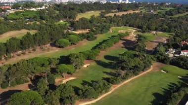 Yemyeşil golf sahasının hava aracı görüntüsü. Gün boyunca sarmal yolları ve ağaçlarla birlikte.