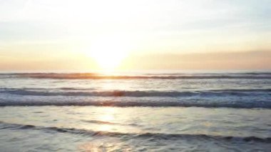 Deniz suyuna yansıyan turuncu gökyüzü ile sersemletici günbatımını gösteren hava aracı görüntüsü. Dalgalar yavaşça çarpıyor. Huzurlu ve huzurlu bir atmosfer yaratıyor.