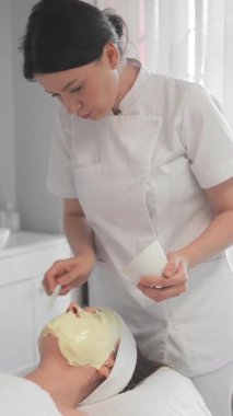Yetenekli bir kozmetikçi müşterisine nemlendirici bir yüz maskesi takar, güzelliğini arttırır ve rahatlatıcı bir klinikte spa deneyimi sağlar..