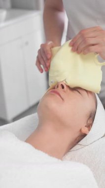 Kadın müşteri kozmetoloji kliniğinde rahatlatıcı bir cilt tedavisi görüyor. Yetenekli bir profesyonel cilt sağlığını ve güzelliğini iyileştirmek için canlandırıcı bir yüz maskesi takıyor..