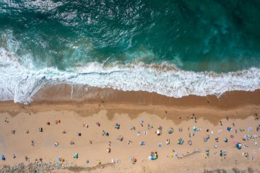 İsimsiz turistlerin ve kumlu deniz kıyısındaki renkli şemsiyelerin insansız hava aracı görüntüleri güneşli bir günde kumsalda yaz tatillerinin tadını çıkarıyor. 