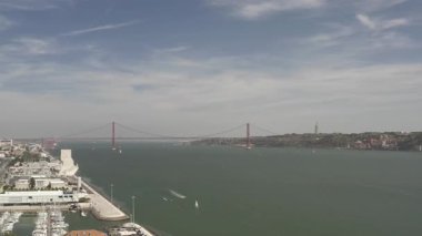 Aerial drone pan left shot of the 25 April Bridge spanning over the Tagus River in Lisbon, Portugal, showcasing the iconic bridge and surrounding cityscape