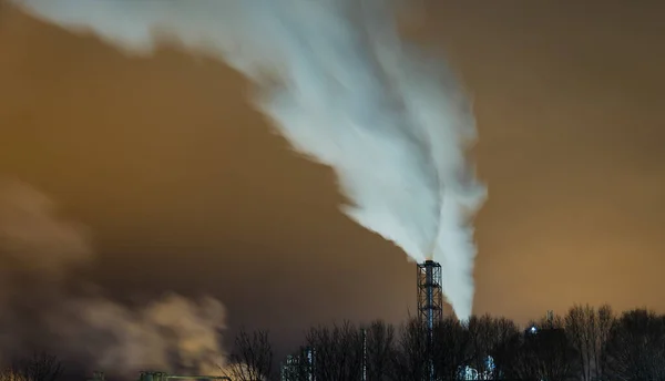 Smoke from a chimney at night in the city above a large industrial facility. Atmospheric pollution.