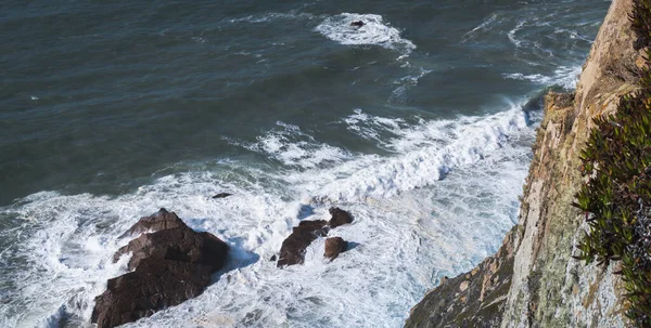 Top view of ocean shore waves forming white foam against the rocks