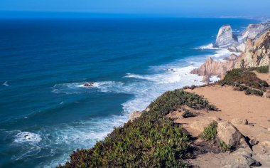 Okyanus kıyısı dalgaları kayaların üzerinde beyaz köpük oluşturuyor.