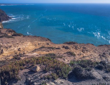 Okyanus kıyısı dalgaları kayaların üzerinde beyaz köpük oluşturuyor.