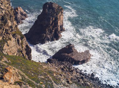 Okyanus kıyısı dalgaları kayaların üzerinde beyaz köpük oluşturuyor.