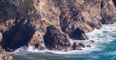 Okyanus kıyısı dalgaları kayaların üzerinde beyaz köpük oluşturuyor.