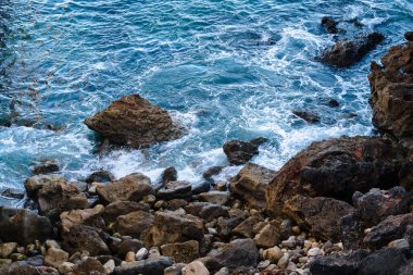 Okyanus kıyısı dalgaları kayaların üzerinde beyaz köpük oluşturuyor.