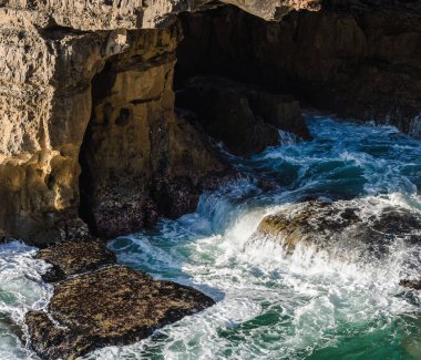 Okyanus kıyısı dalgaları kayaların üzerinde beyaz köpük oluşturuyor.