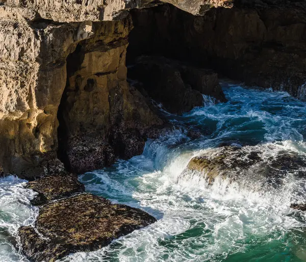 Okyanus kıyısı dalgaları kayaların üzerinde beyaz köpük oluşturuyor.
