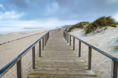 Okyanus kıyısındaki kum tepeleri boyunca uzanan korkuluklu tahta bir yaya geçidi..