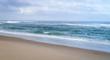 Atlantik Okyanusu 'nun dalgaları kumlu sahili yıkıyor, ufuk görünür durumda, gün bulutlu..