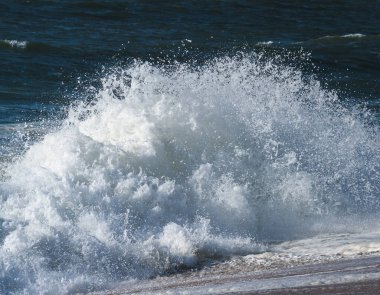 Sahilde köpüren beyaz okyanus dalgaları, arka planda mavi su..