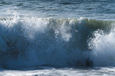 Sahilde köpüren beyaz okyanus dalgaları, arka planda mavi su..