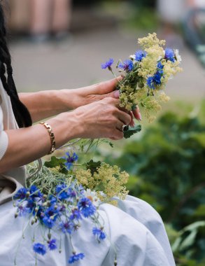 Bir kadının elleri bir çelenk örer, bir yaz gündönümü geleneği, bir çiçek çelengi ve diğer kır çiçekleri, çelenk yapma süreci.