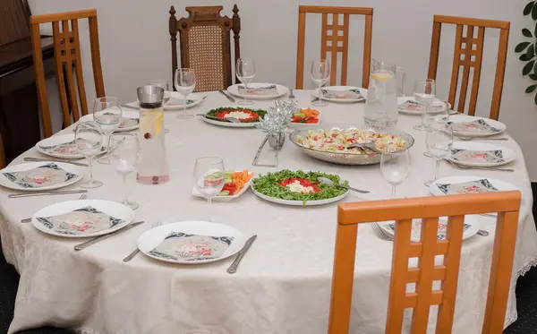 Yuvarlak masa tabaklar ve aksesuarlarla servis edilir, bazı atıştırmalıklar ve içecekler hazır, masanın etrafında sandalyeler.