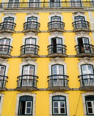 Şehirde birçok pencere ve balkonu olan sarı bir evin ön cephesi, Lizbon, Portekiz