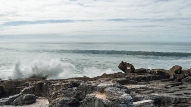 Atlantik Okyanusu dalgaları kayalık kıyılara karşı beyaz köpüğü kamçılıyor, Ericeira, Portekiz.