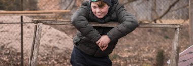 Genç bir Avrupalı çocuk, bir bahar gününün erken saatlerinde, keyifli, kahverengi ceketli ve gri şapkalı..