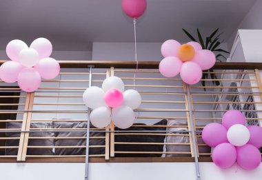 Bir çocuğun doğum günü partisi için evin ikinci katının korkuluklarını süslemek için pembe ve beyaz balonlardan yapılmış çiçekler..