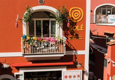 Positano, İtalya - 27 Nisan 2025: Beyaz balkon çeşitli şeylerle süslenmiş. Parlak turuncu bir ev. Amalfi Sahili, İtalya.