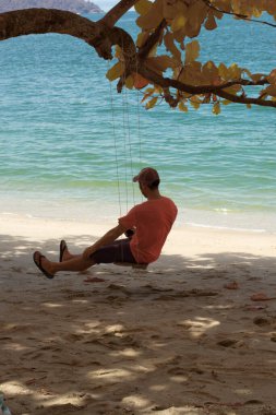 Bilinmeyen bir adamın kızılötesi görüntüsü ağacın altındaki tek halat bankta tek başına oturuyor.