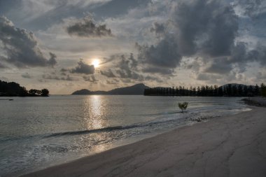 Sakin, ıssız bir sahilde bulutlu bir gün batımı..