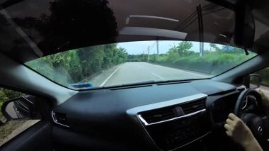 Perak, Malaysia. January 15,2023: Footage of the asphalt street in the countryside while driving in the interior and looking out the car front screen window along the Teluk Senangin to Lumut highway.