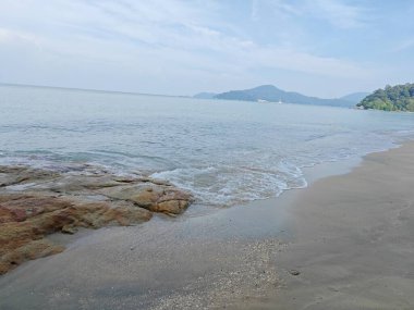 Kumlu sahil boyunca uzanan kaya manzarası.   