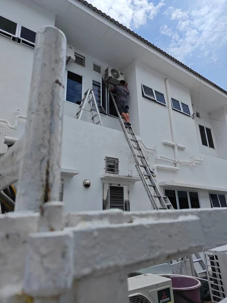 stock image Perak, Malaysia. July 4th, 2023: Worker climbed high up to the second storey building servicing the outlet air condition unit at Taman Mas 1 residence, Kg Koh.