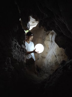 Erkek model, karanlık mağaranın içinde elinde parlak bir kristal küre tutuyor..