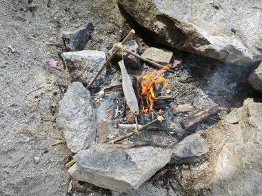 Kaya kenarındaki sahil kenarında kamp ateşinde balık pişiriyorum..