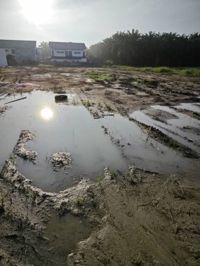 Yerleşim yerinin yakınındaki durgun çamurlu yağmur suyu havuzu boş görünüyor..