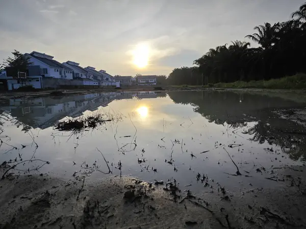 stock image scene of a vacant reflective pool of stagnant muddy rainwater land by the residential area.