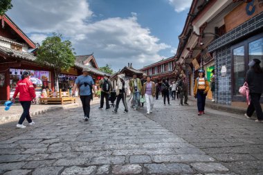 Yunnan, Çin. 30 Nisan 2024: Eski LiJiang kentindeki ünlü UNESCO antik kasaba mirasında turistlerin vitrinlere alışveriş yaptığı ve ticari mallar aradığı gündüz saatleri.